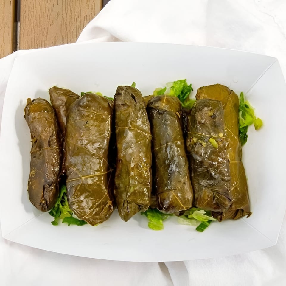 Six dolmades, or stuffed grape leaves, served on a bed of lettuce in a white container.