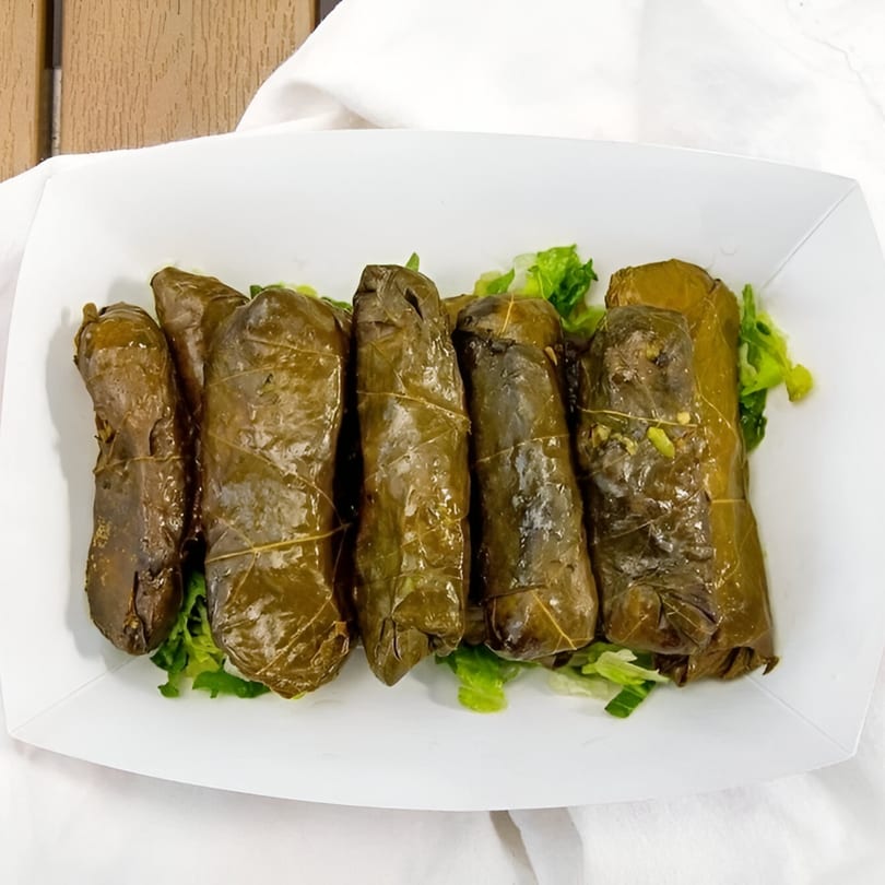 Six dolmades, or stuffed grape leaves, served on a bed of lettuce in a white container.