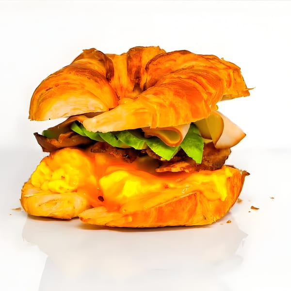 Croissant sandwich with turkey, lettuce, pickles, bacon, and a runny egg with sauce.
