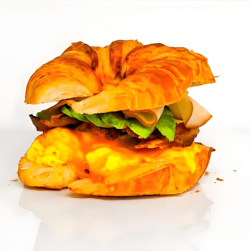 Croissant sandwich with turkey, lettuce, pickles, bacon, and a runny egg with sauce.