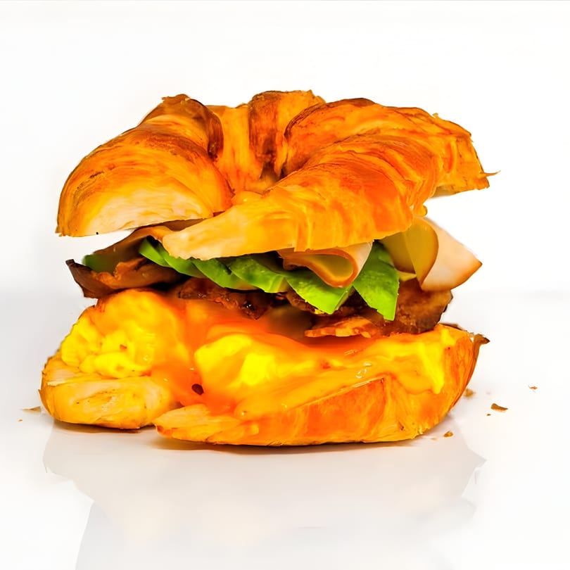 Croissant sandwich with turkey, lettuce, pickles, bacon, and a runny egg with sauce.