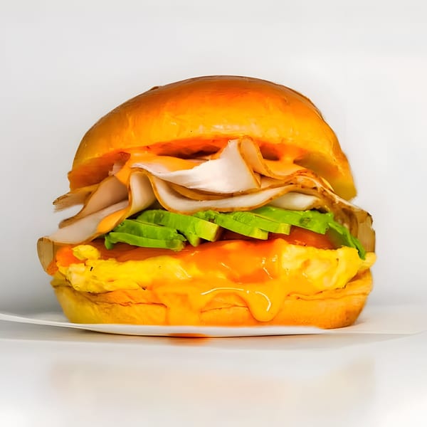 A Gyro 101 breakfast sandwich with turkey, avocado, scrambled eggs, and sauce on a bun.
