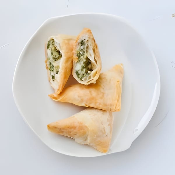 Three golden-brown spanakopita pastries, one cut open to reveal a savory spinach and feta filling.