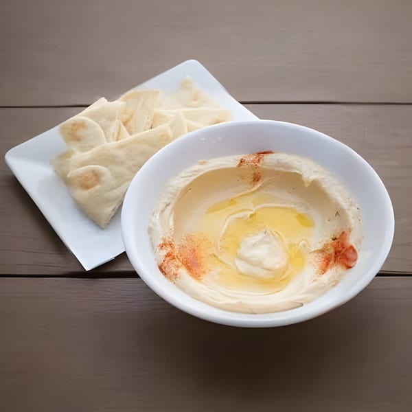 Creamy hummus drizzled with olive oil and paprika, served with pita bread on a wooden table.