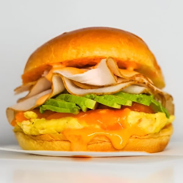 Gyro 101's breakfast sandwich with scrambled eggs, turkey, avocado, and sauce on a bun.