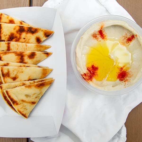 Gyro 101's hummus with olive oil and paprika, served with triangular pita bread in a white tray.