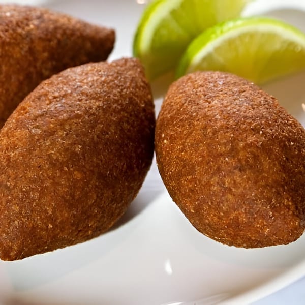 Three golden-brown kibbeh on a white plate, garnished with fresh lime wedges.