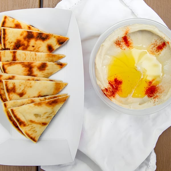 Pita bread triangles in a white container next to a tub of hummus drizzled with olive oil and paprika.