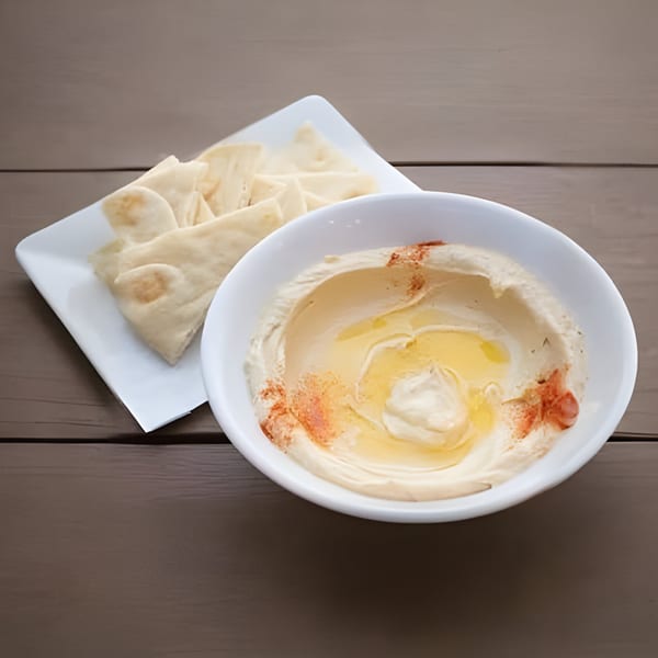 Creamy hummus with olive oil and paprika, served with pita bread on a wooden table.