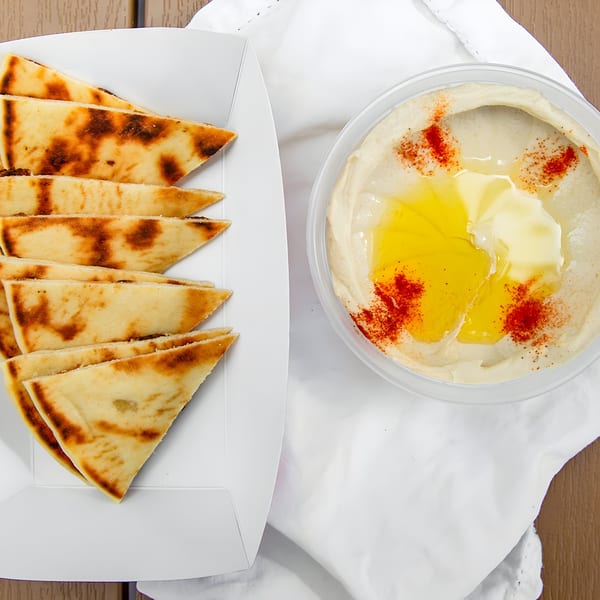 Pita bread triangles in a white tray next to a container of hummus drizzled with olive oil and paprika.