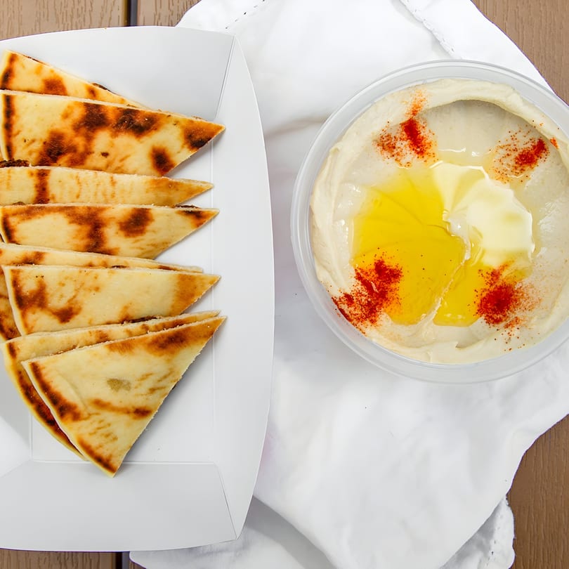 Pita bread triangles in a white tray next to a container of hummus drizzled with olive oil and paprika.